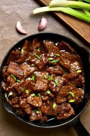 Beef stewed in soy sauce with spices in asian style on brown background with copy space. Mongolian beef. Top view, flat lay